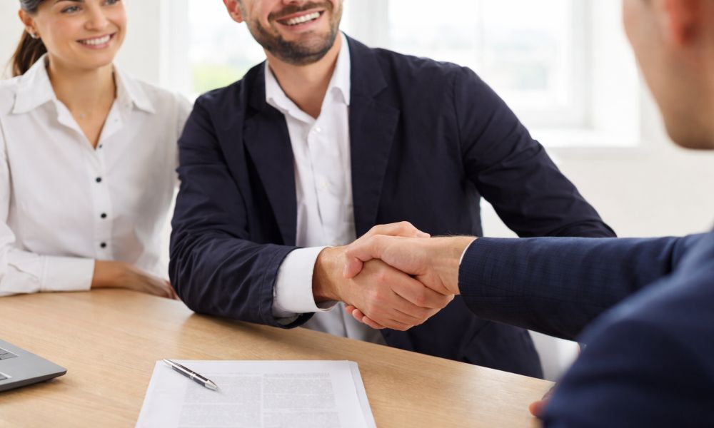 Kupac i prodavac se rukuju preko stola uz ugovor, simbolizujući dogovor o uslovima i roku primopredaje stana