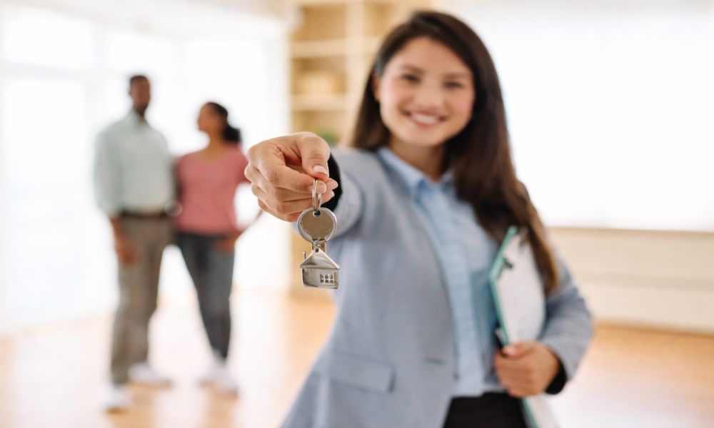 Agent za nekretnine pruža ključ stana dok kupci u pozadini razgledaju prostor i donose konačnu odluku